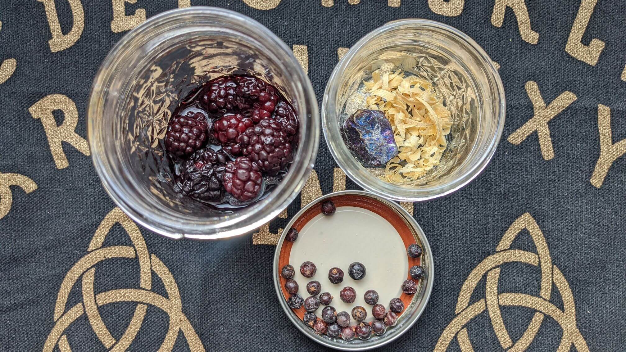 Thawed blackberries, dried juniper berries, and shaved palo santo wood sit in jars on a Ouija board cloth.