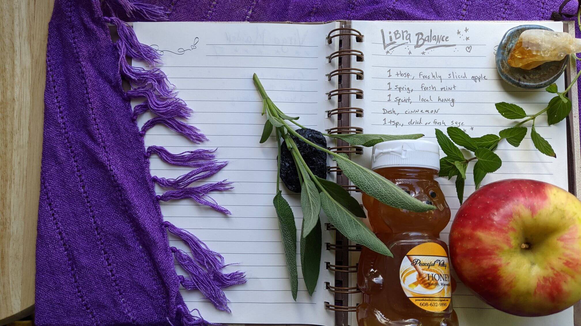 The handwritten recipe is displayed in an open notebook adorned with fresh sage and a bear-shaped jar of honey.