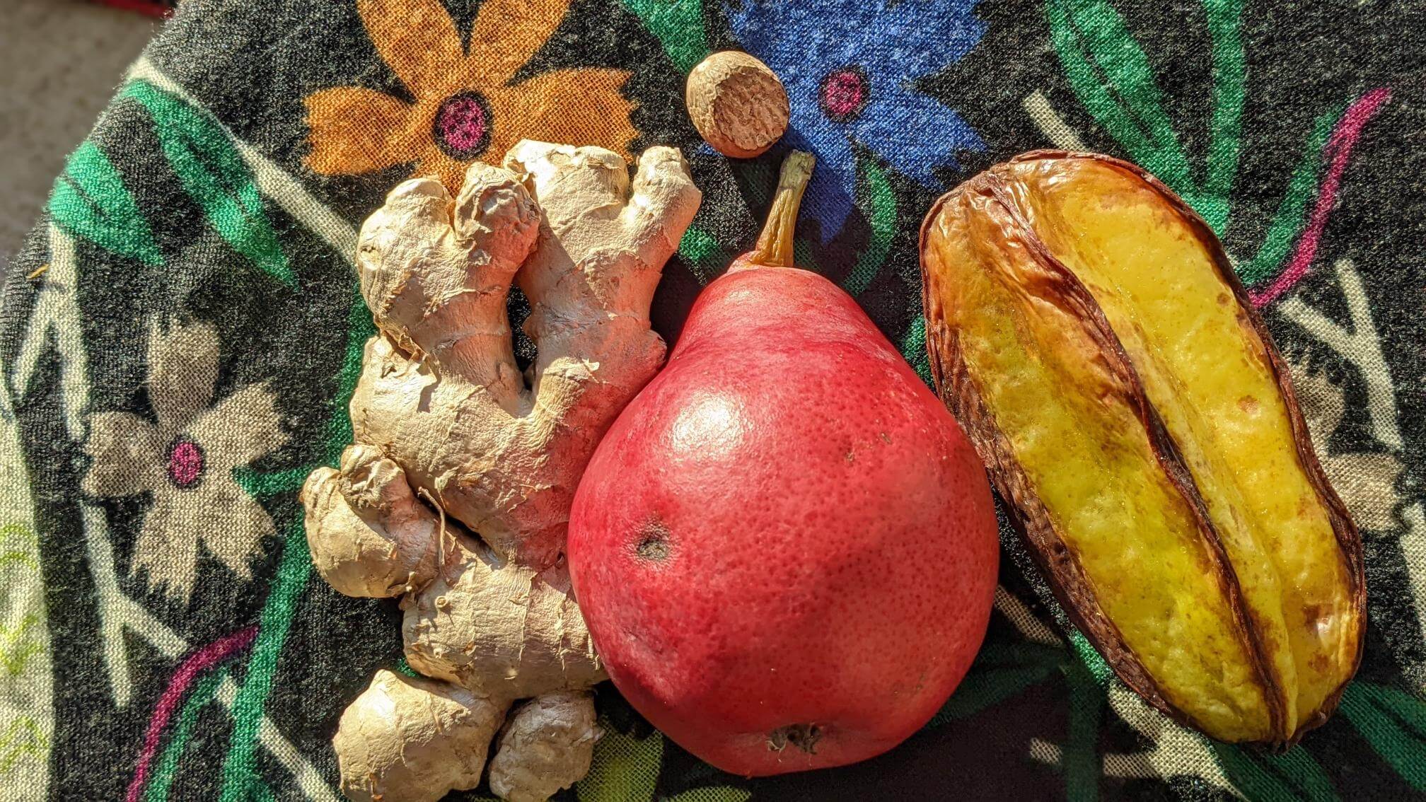 A fresh pear, ginger, and starfruit appear on a multi-color scarf in natural light.